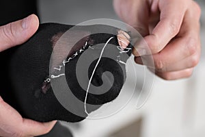 A man sews a black torn sock with white threads. Closeup.  on a white background