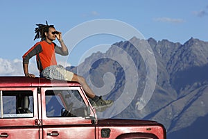 Man Shading Eyes On Top Of Jeep Near Mountains