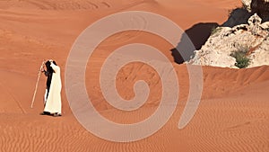 A man in shaman's clothes walks on the sand of the desert with a staff in his hands