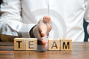 A man shares with his hand cubes with the inscription team. Dividing the collective into two parts or disbanding the team. Lack