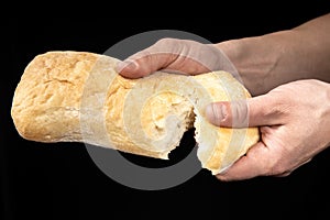 Man is sharing fresh bread ciabatta on black background. Two hands.