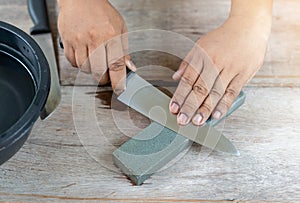 The man sharpen kitchen knife with whetstone on wooden table