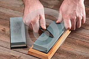 Man sharpening his jackknife with a whetstone on a rustic wooden table