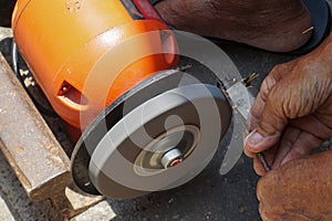 A man is sharpening iron using an orange-colored grinding machine
