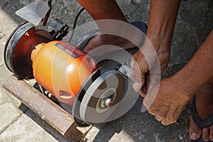 A man is sharpening iron using an orange-colored grinding machine