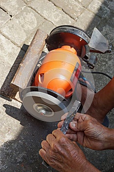 A man is sharpening iron using an orange-colored grinding machine
