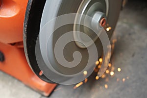 A man is sharpening iron using an orange grinding machine