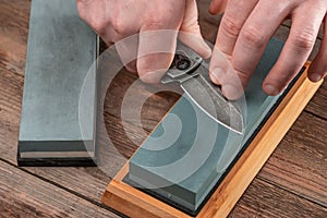 Man sharpening a jackknife with a whetstone on wooden background