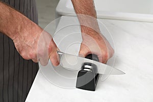 Man sharpening knife at white table, closeup