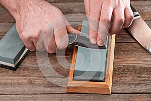 Man sharpens his knives with a whetstone on a rustic wooden table