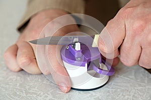 Man sharpens a kitchen knife with sharpener on the table