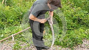 man sharpens an old scythe in the field. Slow motion