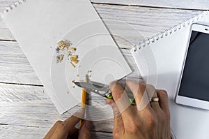 Man sharpens a pencil with a knife in the workplace. Texture and white background.
