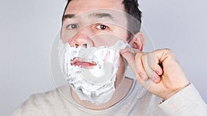 A man shaves his beard and mustache close-up on a gray background. Stop motion.