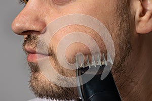 A man shaves his beard with a trimmer razor. Modeling beard, masculine style, facial hair care, morning routines in the bathroom
