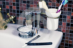 Man shaving accessories safety razor, straight razor, cup with foam and brushes on the sink, mosaic tile background.