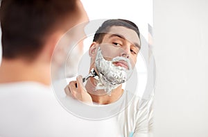 Man shaving beard with razor blade at bathroom
