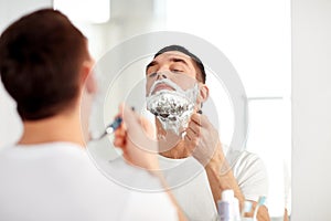 Man shaving beard with razor blade at bathroom