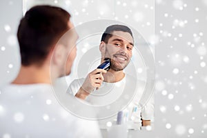 Man shaving beard with trimmer at bathroom