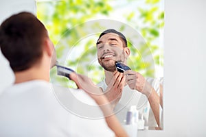 Man shaving beard with trimmer at bathroom