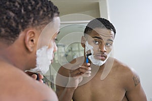 Man Shaving In Front Of Bathroom Mirror