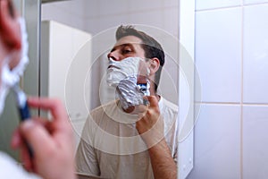 Man shaving with razor and shaving cream in bathroom