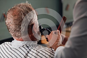 Man shaving senior man`s beard