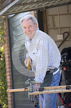 Man at shed sawing wood and smiling