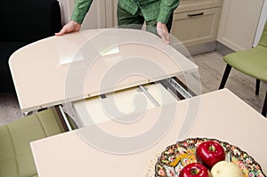 Man shifts a sliding glossy dining table on which stands a plate with artificial fruit