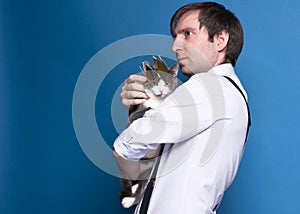 Man in shirt and black suspenders looking into distance, holding and stroking grey cat