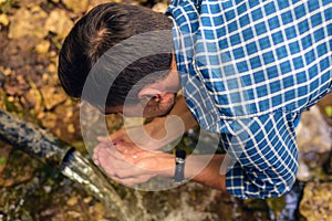 A man in a shirt in a cage collects fresh water from a spring in folded hands, drink water from a source