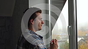 A man in a shirt drinks water standing by the window