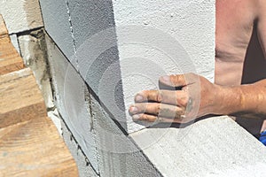A man without a shirt, in hot weather, lays autoclaved aerated concrete blocks on the wall of the house. Build yourself