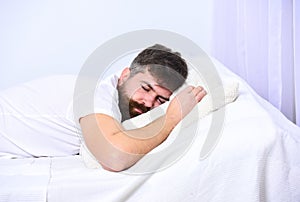 Man in shirt laying on bed, white wall on background. Guy on calm face sleeping on white sheets and pillow. Macho with