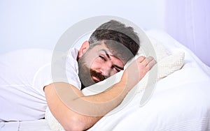 Man in shirt laying on bed, white wall on background. Macho with beard and mustache sleeping, relaxing, having nap, rest