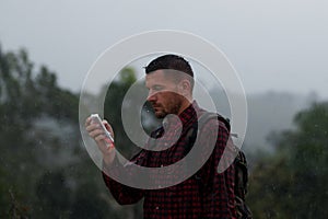 man in a shirt in the rain on nature, use cellphone in cellophane.