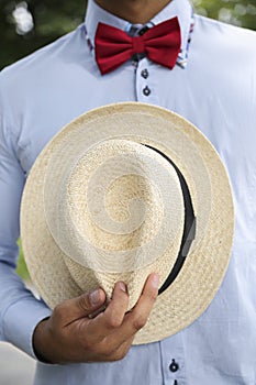 Man in shirt, red bow-tie holding white wicker hat