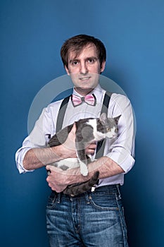 man in shirt, suspender and pink bow tie looking at camera, smiling  and holding cute grey cat