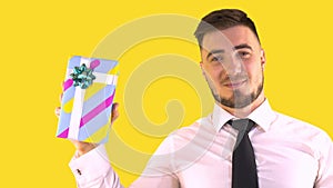 A Man in a Shirt and Tie Shakes a Box with a Gift on a Yellow background.