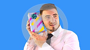 A man in a shirt and tie is trying to understand what is in the box with a gift on a blue background