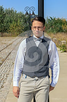Man in shirt and vest with bow tie and glasses, standing leaning