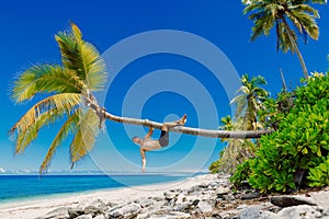 Man shirtless on the beach and climbs a coconut palm tree. Slim man vacation on paradise beach