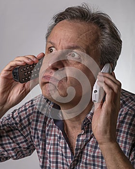A man with a shocked expression listens to two phone calls from two different cordless phones which he holds one in each ear