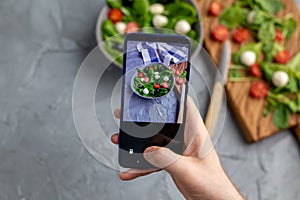 Man shooting fresh vegetable salad with mozzarella and spinach on cell phone camera. Cooking, blogging and healthy