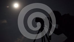 Man shooting the night cloudy sky under moon with a tripod