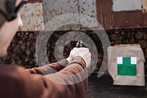 A man shoots a gun, aiming at the target. A man wearing protective headphones. A wall and a roof with bullet holes. outdoor
