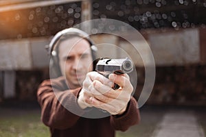 A man shoots a gun, aiming at the target. A man wearing protective headphones. A wall and a roof with bullet holes. outdoor