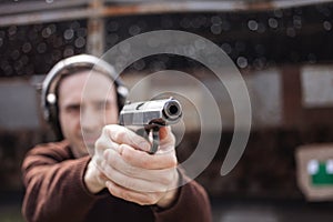 A man shoots a gun, aiming at the target. A man wearing protective headphones. A wall and a roof with bullet holes. outdoor
