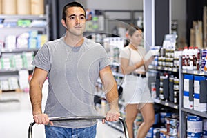 Man shoppers stand with trolley filled with goods for repair and coloring in supermarkets sales hall