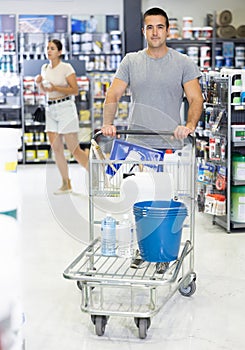 Man shoppers stand with trolley filled with goods for repair and coloring in supermarkets sales hall